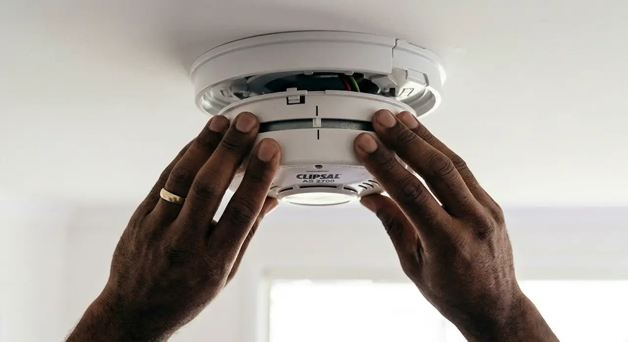 A licensed electrician installing a smoke alarm in a Perth home.